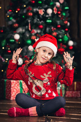 Santa girl wrapped in garland sitting on floor.