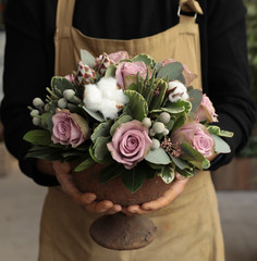 Festive flower arrangement of paleviolet roses and cotton flowers in the vase florist holding at...