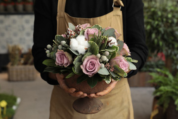 Festive flower arrangement of paleviolet roses and cotton flowers in the vase florist holding at...