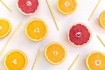Orange and grapefruit slices lying on alight background with juice straws among them.