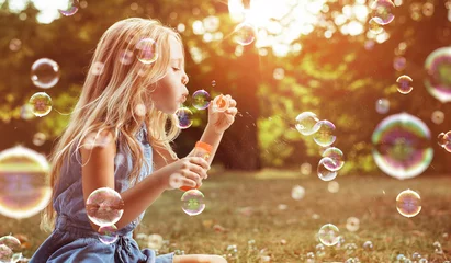 Foto op Plexiglas Portret van een vrolijk meisje dat zeepbellen blaast © konradbak