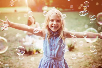Poster Im Rahmen Cheerful little girl enjoying bubble blowing © konradbak