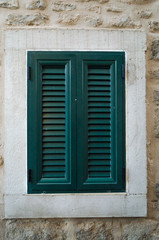 One window with closed green shutters on the background of beige wall.