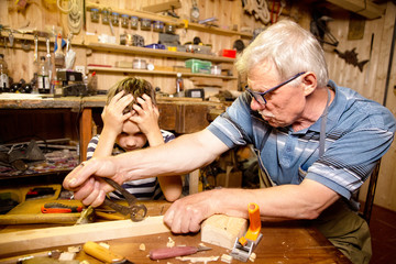 grandfather and grandson in the carpentry workshop. the old carpenter fixes the work of the student