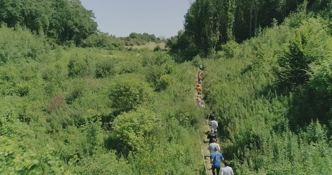 Aerial shot of people running a competition on a trail in a small valley through the woods during summer.