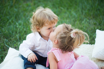 Girl kiss boy with blond hair on green grass
