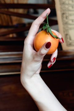 A womans hand holding a small christmas orange between her thunb and first finger