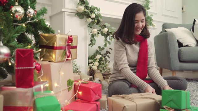 Cheerful happy young Asian woman packing and wrapping Christmas present decorate her living room at home in Christmas Festival. Lifestyle woman celebrate Christmas and New year concept.