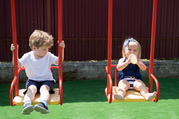 Playing is fun. Small brother and sister enjoy playing together. Small children with blond hair on swing. Girl and boy haircut styles. Hair salon for children. Haircut, always going to be in style
