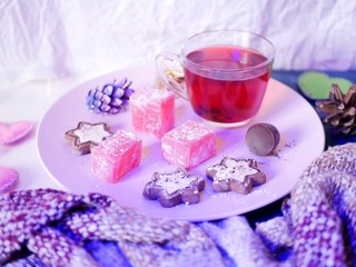 On a pink dish, sweets, chocolate cookies, tea, on the table decor of Christmas tree decorations, fluffy scarf, felt hearts. Evening illumination, top view, concept of seasonal winter holidays, christ