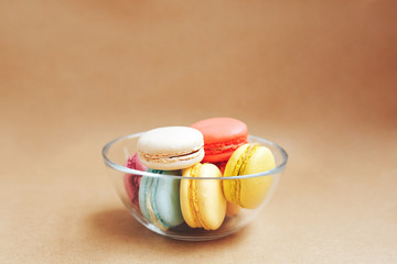 transparent bowl with multi-colored macaroons on kraft brown backgrownd