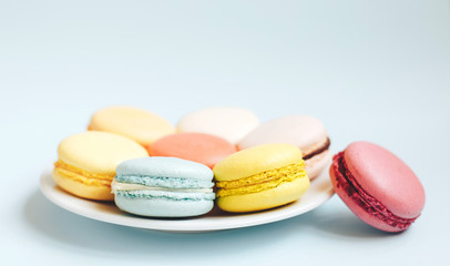 multicolored macaroons on a plate on light blue background