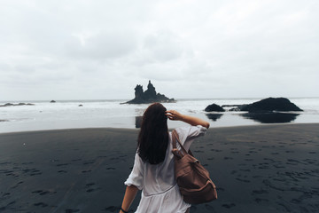 Young girl walking on the beach and looking at the ocean in the cloudy evening Benijo, Tenerife, Spain