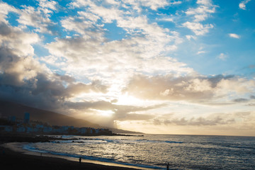 Fototapeta na wymiar Beautiful cloudy sunset on the beach with resting people in Puerto de la Cruz, Spain