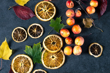 Fototapeta na wymiar Dried sliced lemons and oranges with fresh red apples and autumn leaves on dark texture surface.