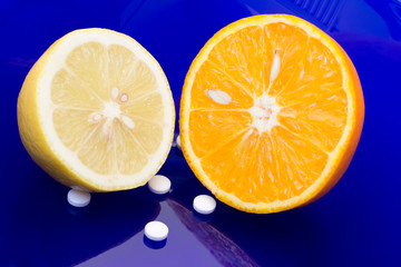 Food-born and synthetic vitamins. Lemon half, orange half and vitamin C tablets on blue background