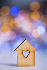 Obraz na płótnie Canvas Wooden icon of house with hole in the form of heart on colorful bokeh background.