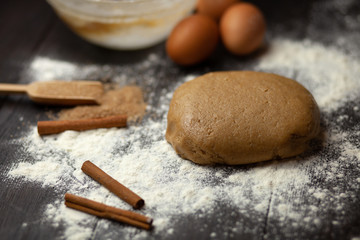 The process of preparing dough for Christmas cookies with cinnamon, ginger and sugar. On a dark brown background sprinkle with flour. Ingredients for cookies. New year's magic. With the blur