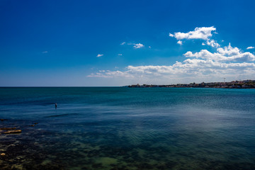 a fisherman fishing in the sea, in the city of Trani, with the Monastery of Santa Maria di Colonna in the background. In Puglia, near Bari, in the province of Barletta, Andria, Trani. Sea and blue sky