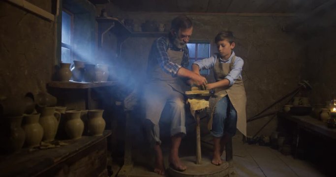 Old Caucasian grandfather teaching and showing his little cute grandson pottery manufacturing.
