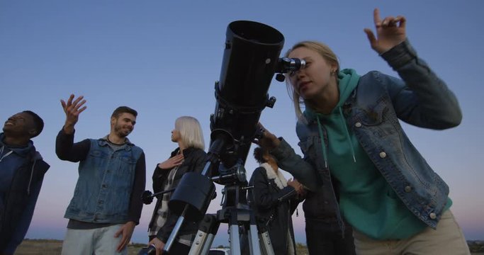 Medium shot of happy adult friends stargazing together and using a professional telescope and pointing at the sky