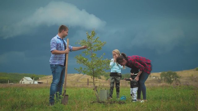 Friendly family, children planting tree with parent in garden.