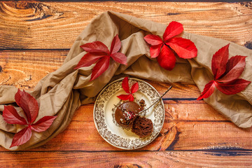 Chocolate muffin on a vintage plate and red leaves on  wooden background