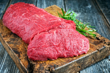 Rohes Roastbeef mit Kräutern angeboten als closeup auf altem rustikalen Schneidebrett