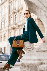 Outdoor full body fashion portrait of young woman wearing sunglasses, white turtleneck, blue suit,...