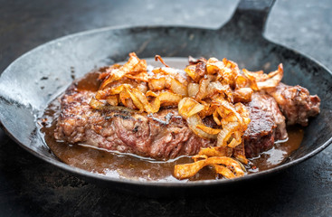 Traditional dry aged sliced roast beef with fried onion rings as closeup in a wrough-iron pan with...