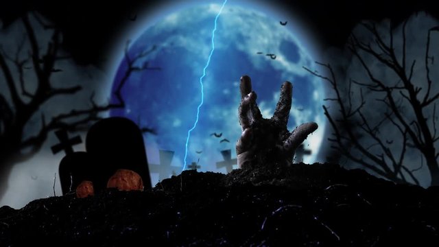 Zombie hand emerges from the grave amid halloween pumpkins and flying bats and the blue moon