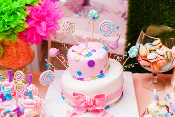 First birthday pink cake with lollypops and one candle for little baby girl and decorations for party