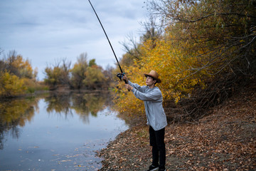 young fisherman in hat fishing with rod in forest lake f