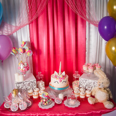 Sweet table and big unicorn cake for baby girl first birthday. Candy bar with a lot of different candies and sweet cakes