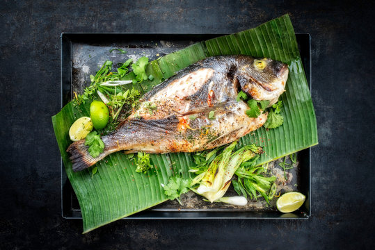 Fresh barbecue gilthead seabream with lettuce and herbs as top view on a green banana leaf