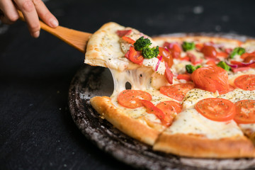 Hot pizza slice with melting cheese on a rustic black table.