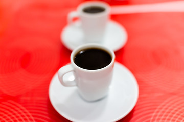 Macro closeup of two espresso dark roast coffee cups with detail, texture of black brown liquid on plate, red background table in Italy cafe breakfast