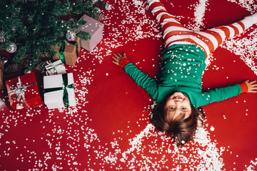 Kid lying on floor beside a christmas tree