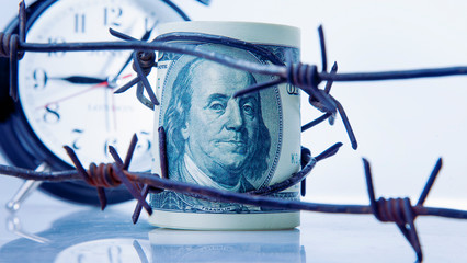 Economic warfare, sanctions and embargo busting concept. US Dollar money, alarm clock and barbed...