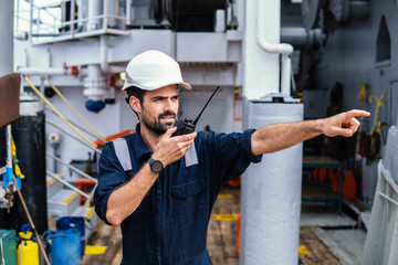 Marine Deck Officer or Chief mate on deck of vessel or ship . He holds VHF walkie-talkie radio in...