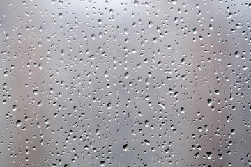 Background with rain droplets on window glass on gloomy autumn day on blur gray background closeup