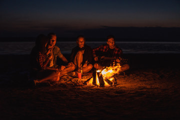 Camp on the beach. Group of young friends having picnic with bonfire. Man is playing guitar