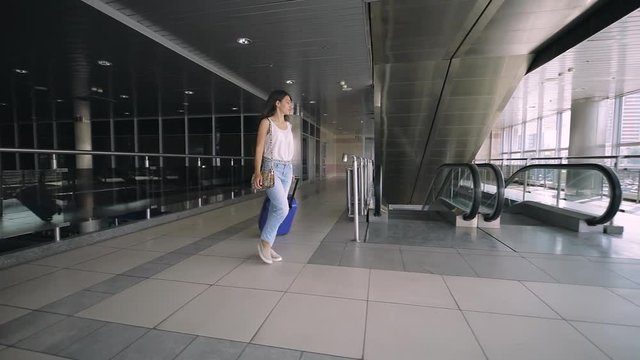 Young brunette woman goes on escalator with travel bag.