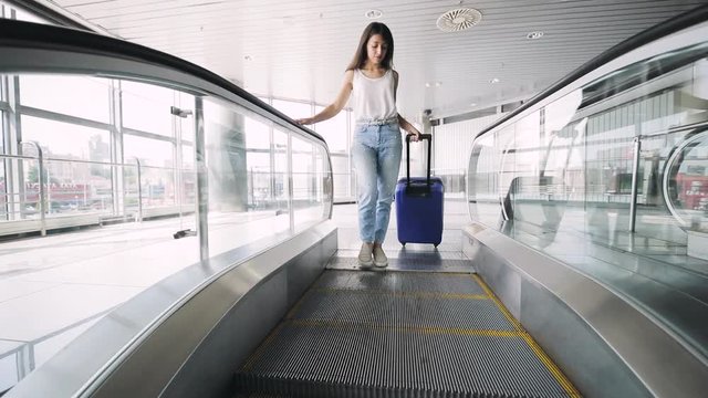 Young brunette woman goes on escalator with travel bag.