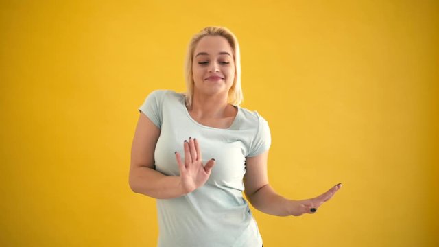 Young blond attractive caucasian plus size model happy dancing at yellow background