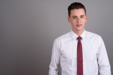 Portrait of young handsome businessman against gray background