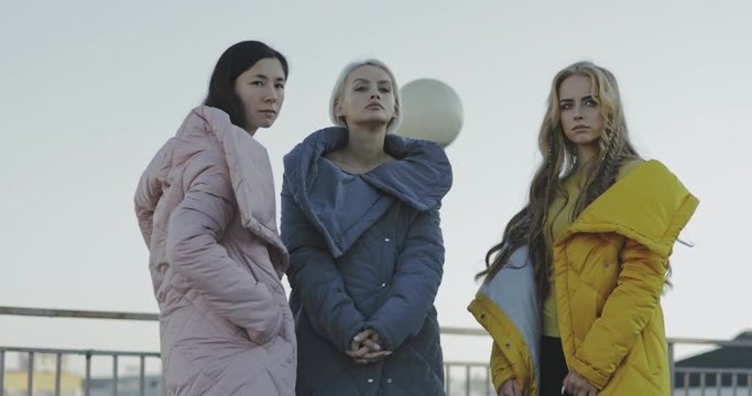 Portrait of three young multiracial women talking and laughing in the street. Female models wearing jeans and long jacket coat. 4k video steadicam shot