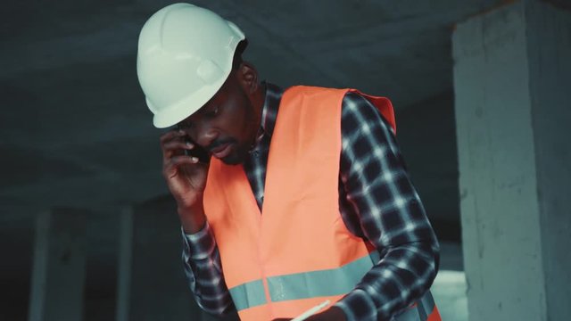Professional afro american male working with building projects blueprint and talking on phone. Being busy, profession concept. Male portrait