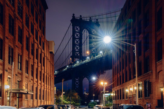 Fototapeta Brooklyn bridge seen from a narrow alley enclosed by two brick buildings at dusk, NYC USA