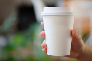 Obraz premium Woman hand holding white paper cup of hot coffee in cafe.